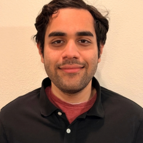 Smiling man with dark hair, light stubble, wearing a black shirt over red.