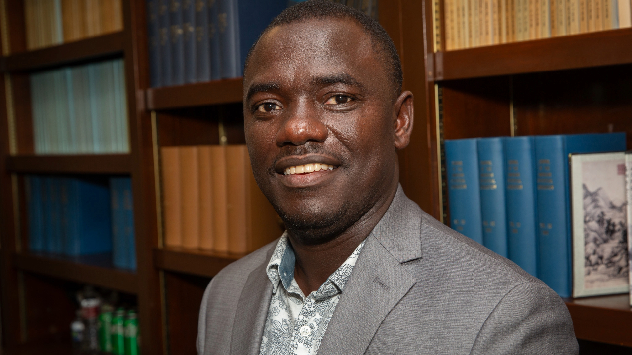Dr. Samuel Kakraba smiling in grey suit jacket in front of a bookshelf.