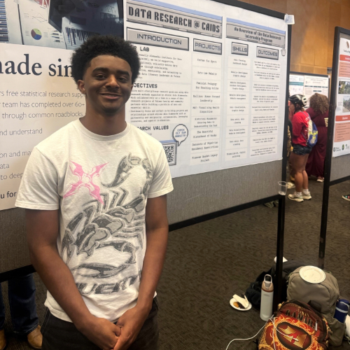 Young man in a graphic tee smiles in front of a poster.
