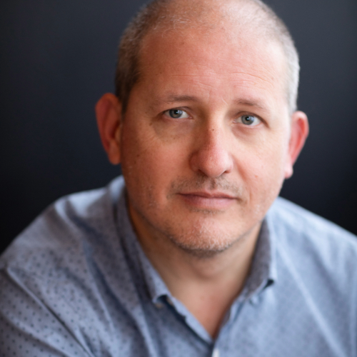 Headshot of a middle-aged man with short, graying hair and a blue patterned shirt.